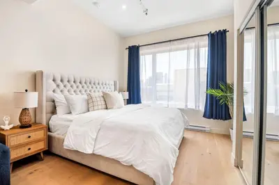 a white bedroom with a large bed with blue curtains at Central King Studio in Montréal