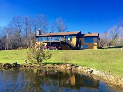 a house on a hill next to a body of water at Spacious luxurious Villa, bright cottage, pool, Jacuzzi, sauna, nature in Mansonville