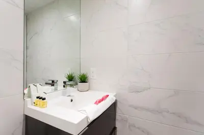 a white bathroom with a sink and a mirror at Scandinavian Studio with Full Kitchen and Bath by Den Stays in Montréal