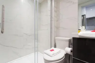 a white bathroom with a shower and a toilet at Blue Oasis Studio with Full Kitchen and Bath by Den Stays in Montréal